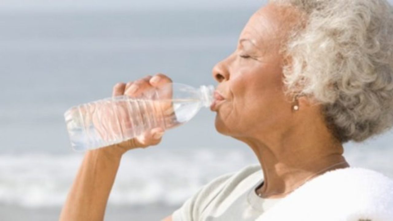 Foto de idosa numa praia tomando água mineral